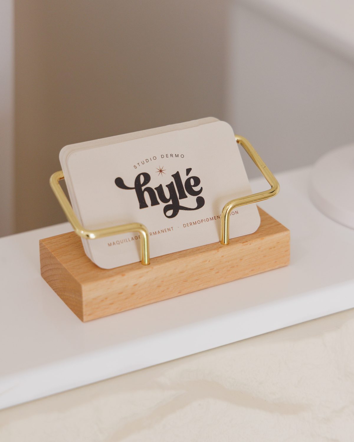 Cartes de visite Hylé Studio Dermo sur un présentoir en bois et laiton