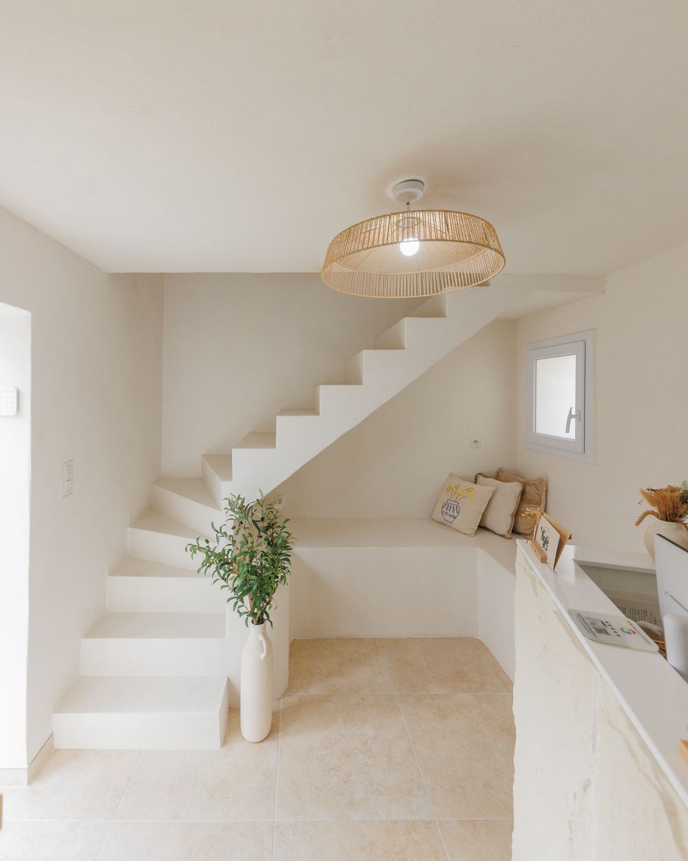 Espace d'accueil lumineux du studio Hylé à Biguglia : escalier blanc, banquette et olivier